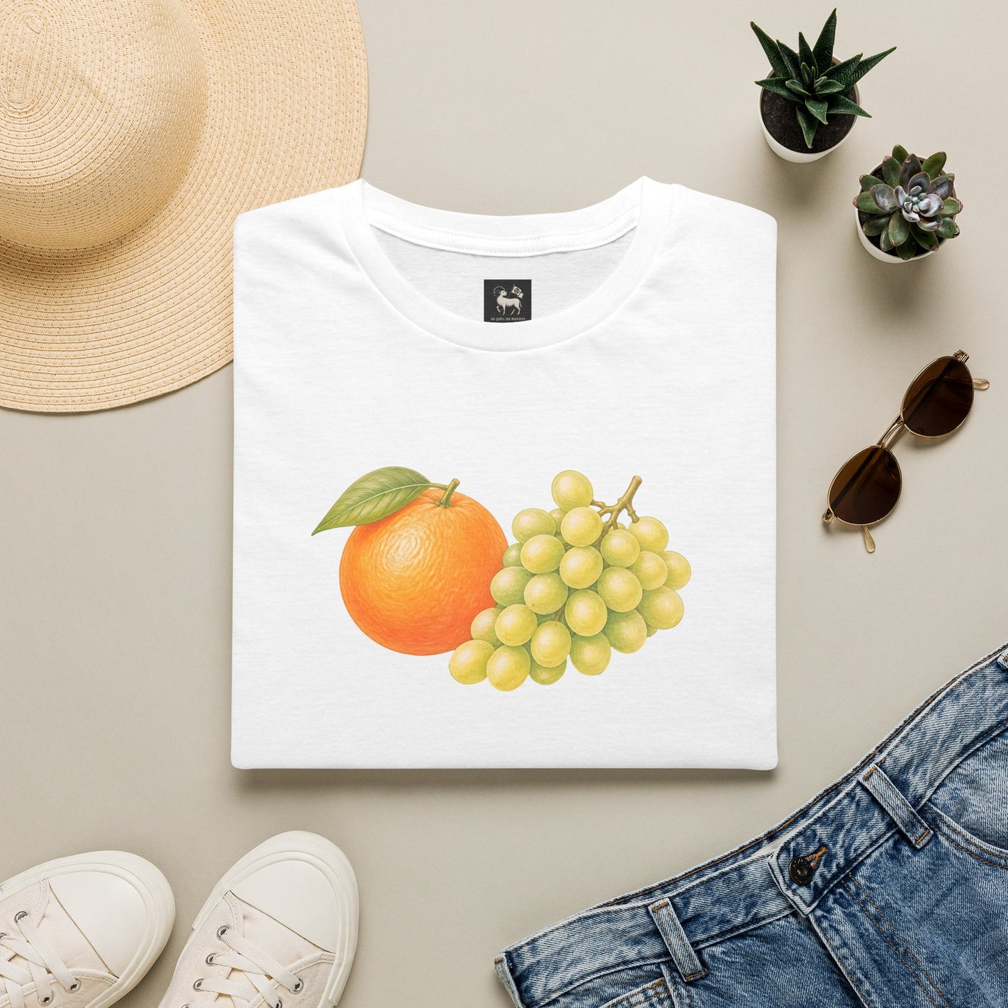 Orange Grapes tee by Unruly Thread — a hand-drawn orange beside a bunch of green grapes, colored-pencil still life on a soft cream ground.